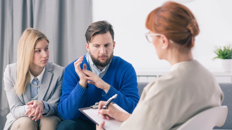 תמונת נושא של המאמר על ייעוץ זוגי לפני נישואין המציג זוג צעיר יושב בלחץ בייעוץ זוגי מול פסיכולוגית או יועצת עם שיער ג'ינג'י המקשיבה ורושמת