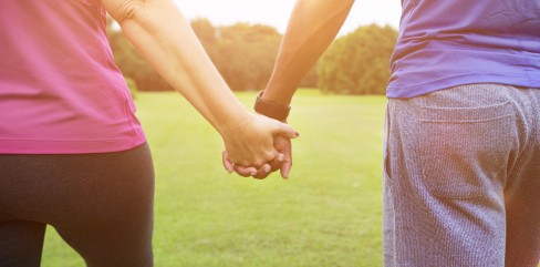 תמונת נושא של המאמר מהי זוגיות בריאה המציגה זוג מחזיק ידיים בעמידה על דשא ירוק כשהשמש שוקעת.