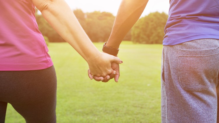 תמונת נושא של המאמר מהי זוגיות בריאה המציגה זוג מחזיק ידיים בעמידה על דשא ירוק כשהשמש שוקעת.