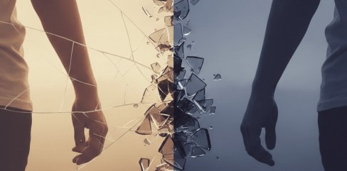 תמונת נושא של המאמר על משבר אמון בזוגיות המציגה צילום אמנותי המציג שתי דמויות עומדות גב אל גב ומופרדות על ידי זכוכית שבורה ומתנפצת במרכז הפריים. הצד השמאלי של התמונה מואר בגוונים חמים של כתום וזהב המזכירים שקיעה, בעוד הצד הימני מוצל בגוונים קרירים של כחול ואפור כהה. רסיסי הזכוכית עפים לכל עבר בקו התפר שבין שתי הדמויות, מה שיוצר תחושה חזקה של פרידה, שבר ביחסים או קונפליקט רגשי. הדמויות נראות רק בחלקן, מה שמעצים את תחושת הניכור והמרחק ביניהן למרות הקרבה הפיזית.