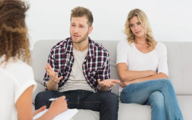 תמונת נושא של המאמר על טיפול זוגי לזוגות צעירים המציגה זוג צעיר יושב על ספה בחדר יועץ זוגי הגבר מדבר בתנועות ידיים והאישה יושבת שלובה ידיים במבט כעוס.