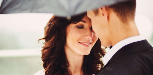 תמונת נושא של המאמר ייעוץ נישואין צילום תקריב של זוג ביום חתונתם עומד בחוץ מתחת למטרייה החתן עם הגב למצלמה והכלה מחייכת בעיניים עצומות