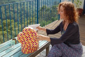 תמונת אווירה של ייעוץ זוגי - אורית צוקרPh.D יועצת טיפולית T.C מציגה אישה עם שיער אדום יושבת במרפסת ומוציאה פתק קטן מתוך קופסת לב מעוטרת.