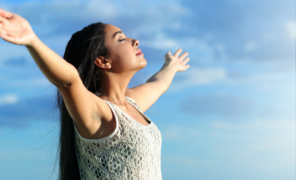 תמונת אווירה מדף הבית של אורית צוקר מטפלת זוגית מציגה אישה מחייכת מניחה ידיים לצדדים מול השמיים עם עננים.